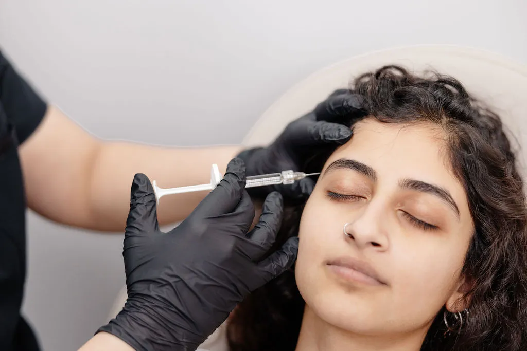 A patient receives a dermal filler injection near the temple